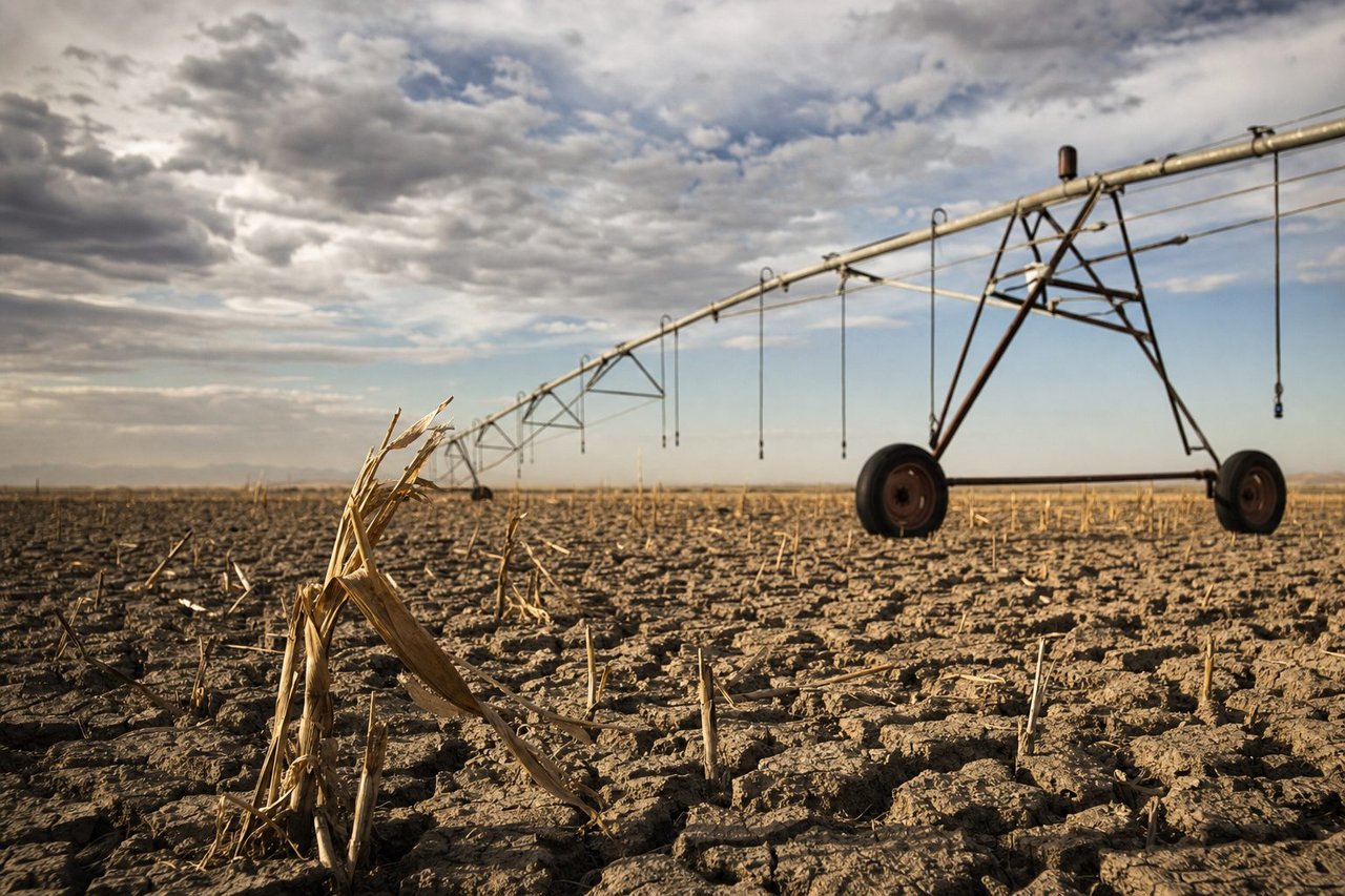 A drought-stricken farm field with deep cracked soil and an idle irrigation sprinkler