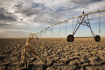 A drought-stricken farm field with deep cracked soil and an idle irrigation sprinkler