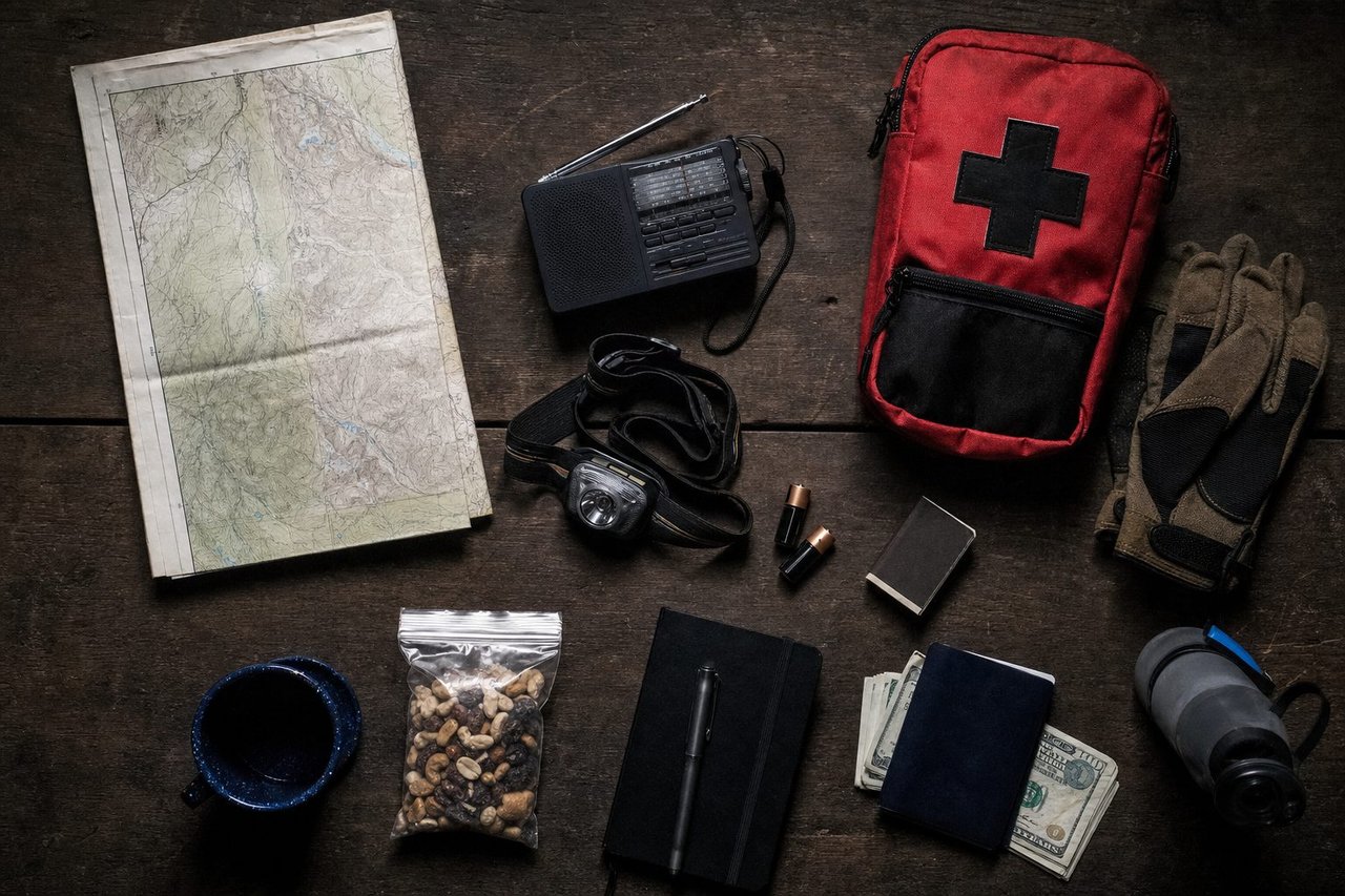 Emergency go-bag contents laid out on a table — water, radio, first-aid kit, flashlight
