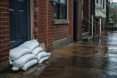 A ground-floor apartment doorway with sandbags stacked against it during steady rain, street-level view